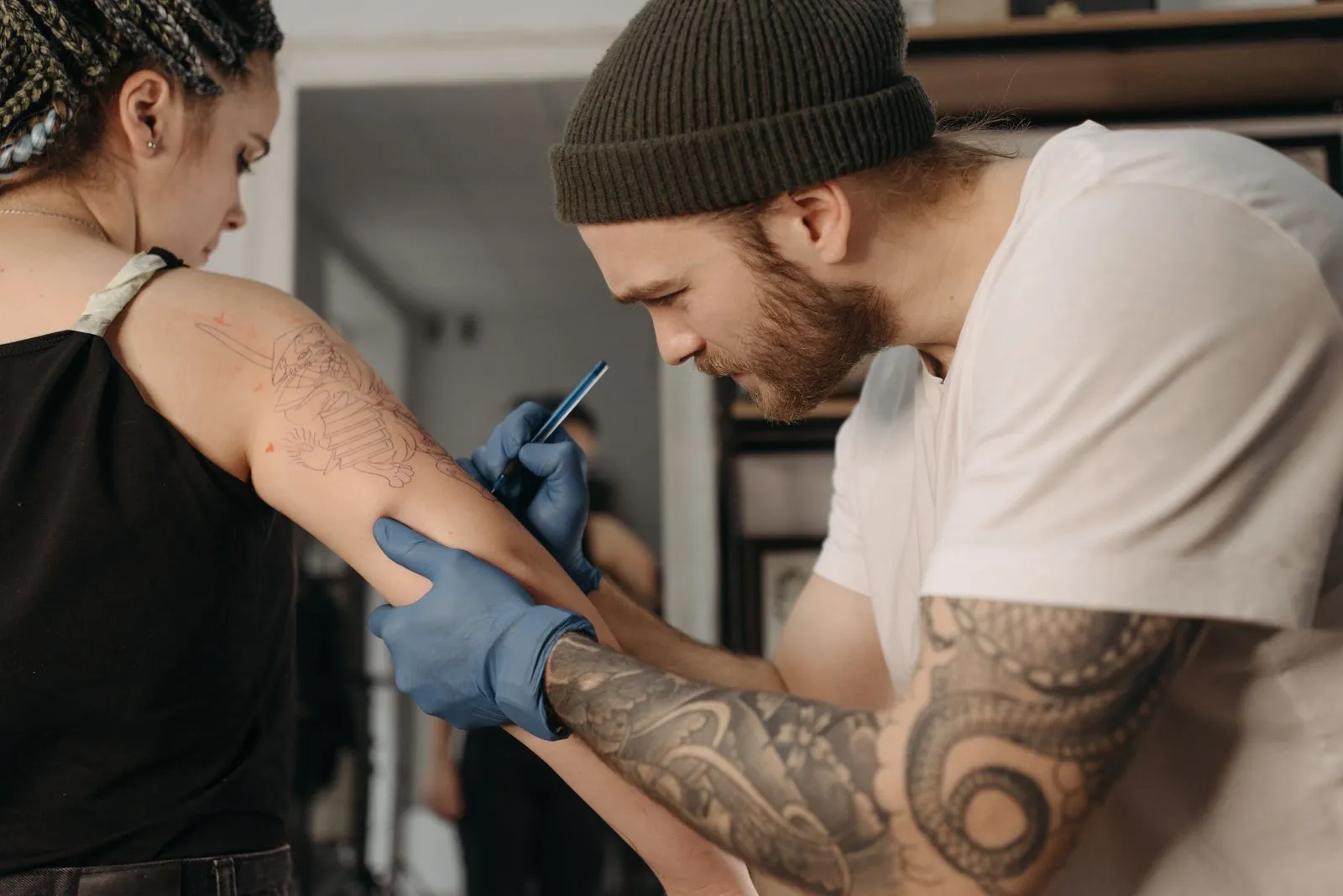 A focused tattoo artist working on an arm tattoo in a studio.